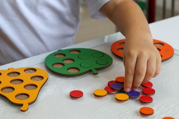 아이는 색깔별로 원을 삽입하는 논리적인 나무 장난감 놀이를 합니다. 교육용 장난감 및 활동