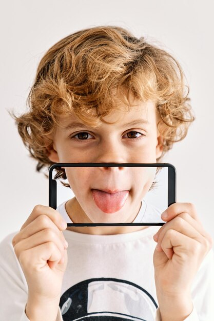 Child posing sticking tongue with his mobile phone and photos made of parts of his face