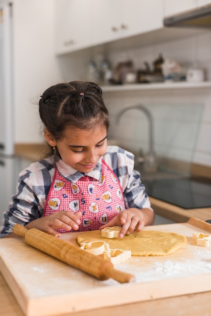 子供はクッキーを準備し、ハートの形に丸められた生地の置物から切り取ります。ハートの形で生の生地からクッキーを作る子供の手、クローズアップ。