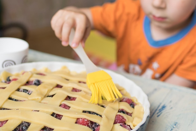 The child prepares a pie The little boy smears the top of the pie