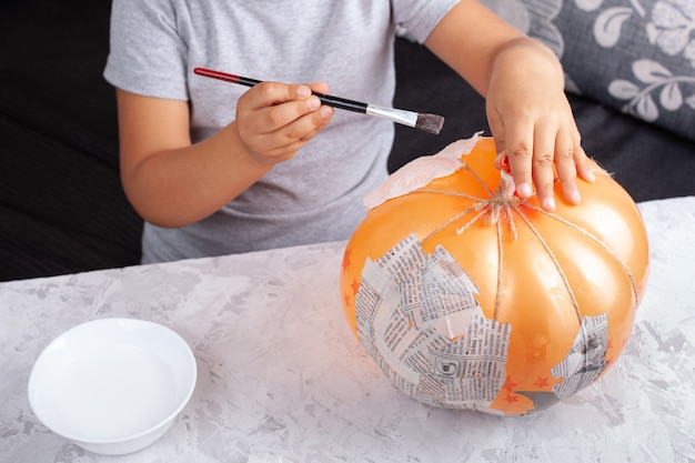 Un bambino mette la colla su un palloncino per attaccare pezzi di carta, fa una zucca con la cartapesta.