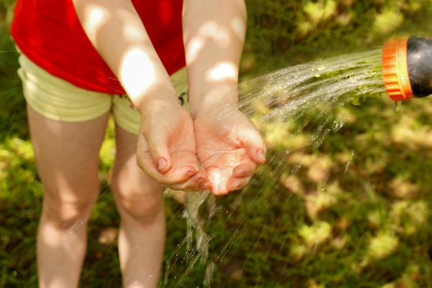 A child puts his hands under water flowing from a watering hose on a warm summer day