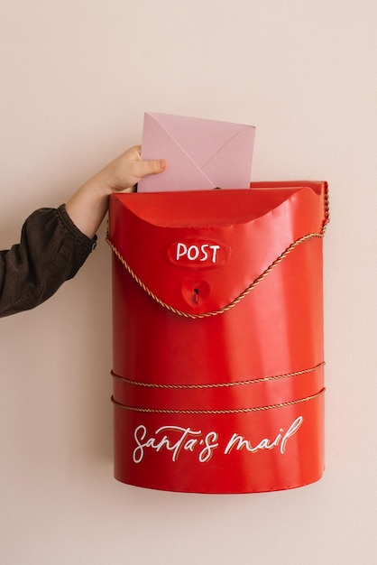 A child puts a letter to Santa Claus in a red Christmas mailbox