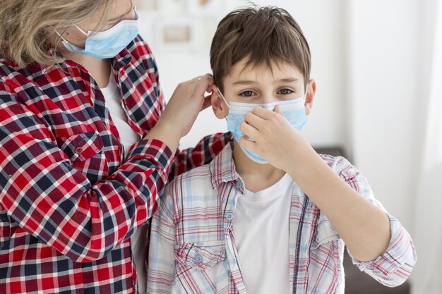 Child putting on medical mask with the help of his mother