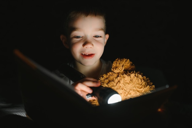 Child reading book in bed Kids read at night Little boy with fairy tale books in bedroom Education for young children Bedtime story in the evening Cute kid under blanket in dark room with lamp