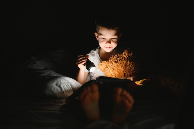 Child reading book in bed Kids read at night Little boy with fairy tale books in bedroom Education for young children Bedtime story in the evening Cute kid under blanket in dark room with lamp
