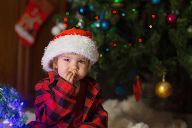 赤い服を着た子供が新年を待って座っています。真夜中にクリスマスを祝うというコンセプト。ホリデーコスチューム