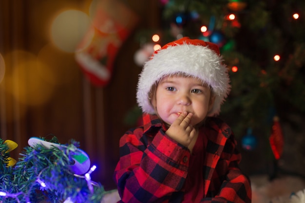 赤い服を着た子供が新年を待って座っています。真夜中にクリスマスを祝うというコンセプト。ホリデーコスチューム