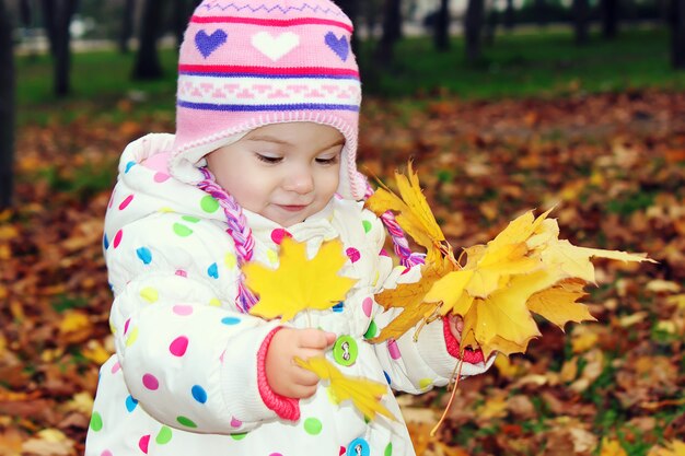 Ребенок в красной шубе с осенними листьями.