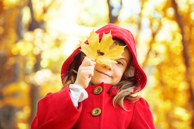 Bambino in un cappotto rosso con foglie di autunno