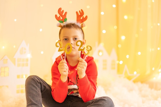 A child in a red knitted sweater with santa's reindeer on the background numbers 2023 on sticks