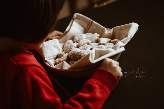 Bambino in maglione rosso guarda un cesto di biscotti ricoperti di zucchero fatti in casa