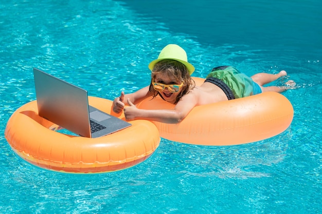 Bambino che si rilassa in piscina con un bambino portatile online che lavora su un computer portatile che nuota in una soleggiata turchese wa