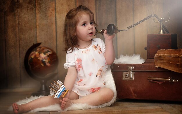Photo a child in a retro interior and an old phone sits on the floor a small child is a traveler in vintage decorations child traveler is calling phone