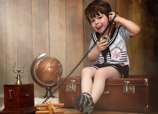 レトロなインテリアの子供と古い電話が床に座っています。小さな子供はヴィンテージの装飾の旅行者です。子供の旅行者は電話で電話をかけています。