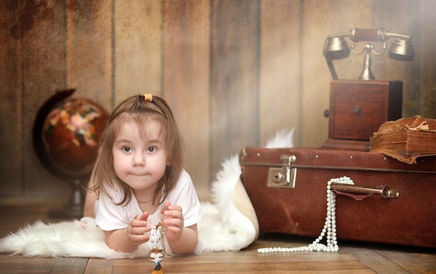 A child in a retro interior and an old phone sits on the floor. A small child a traveler in vintage decorations. Child traveler is calling by phone.