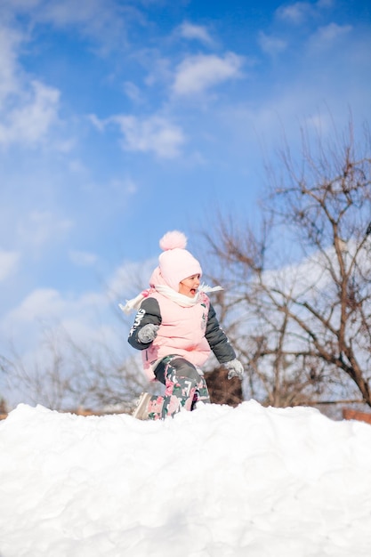 Child rides on snow slide little girl in winter warm suit plays\
in fresh air and enjoys sunny day in winter she lies in snow and\
plays snowballs