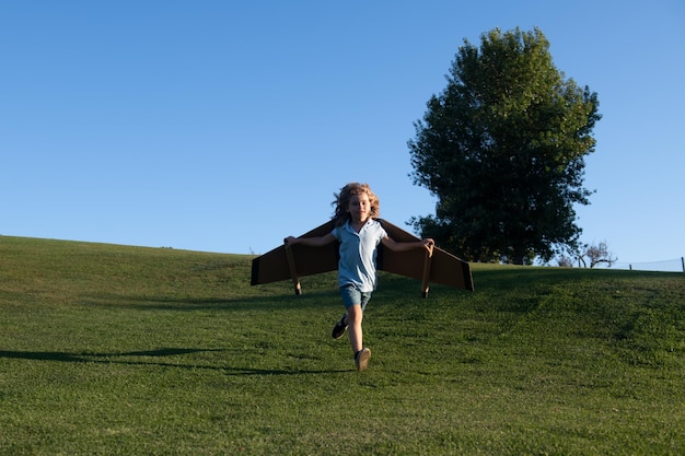 Child running on grass in park Child flying in plane made craft of cardboard wings Dream imagination childhood Travel and summer vacation concept