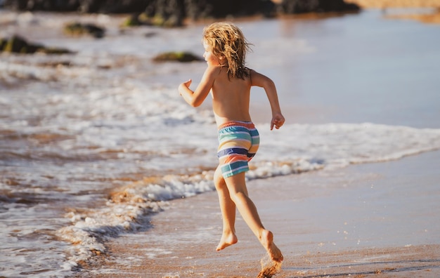 海のビーチに沿って海岸近くの水の中を走っている子供男の子が海岸に沿って走っている残りの部分o