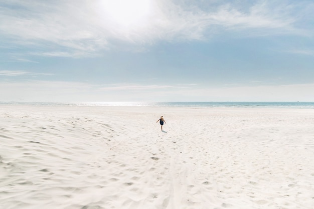 화창한 날씨에 한 아이가 하얀 해변을 따라 발트해로 달려갑니다.