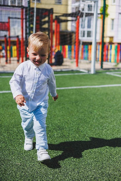 The child runs in the park A boy in a white shirt and trousers Green lawn or field Mowed lawn Walk and play in the forest Active sports