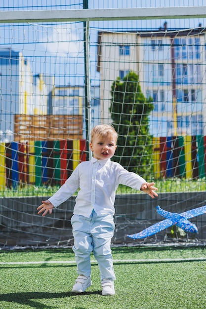 Un bambino corre nel parco con un aeroplano giocattolo un ragazzo con camicia bianca e pantaloni prato o campo verde prato falciato camminare e giocare nella foresta sport attivi