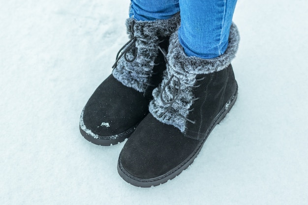 The child's feet in jeans and warm boots on the snow. Beautiful and practical women's winter shoes.