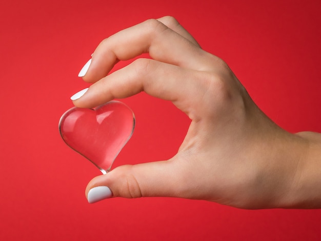 Le dita del bambino tengono delicatamente un cuore di vetro su fondo rosso. un simbolo di amore e vita.