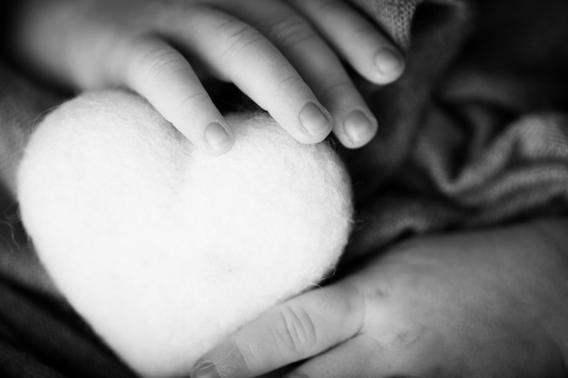 Child's hand, fingers close up. Newborn baby hands, happy childhood concept, healthcare, IVF, hygiene. Newborn holding a soft heart in his hands. Black and white photo.