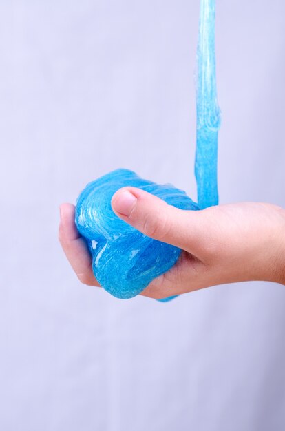 Child's hand holding bright glitter slime. Kid playing with slime, worldwide popular self made toy. Making slime by yourself.