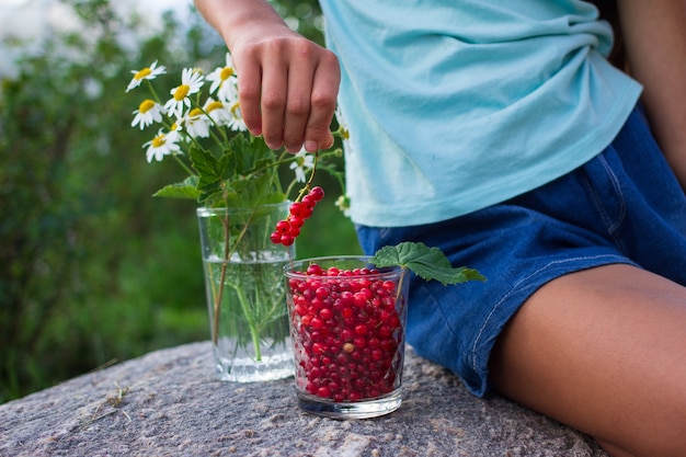 Child's hand holding glass full of red currants in summer outdoors in garden