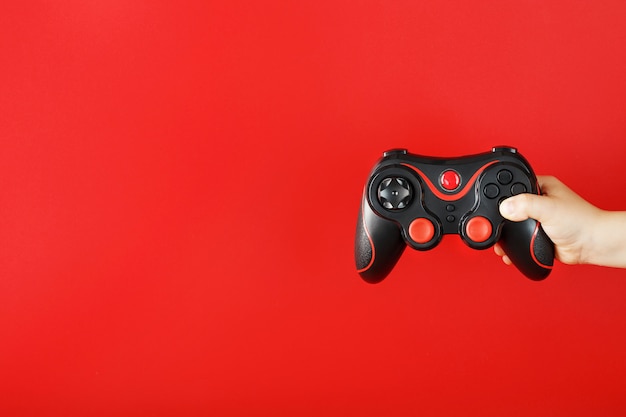 Child's hand holds a gamepad on a red surface