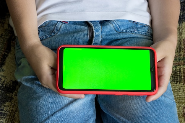 La mano di un bambino tiene uno smartphone in posizione orizzontale con uno schermo verde. chiave cromatica. modello