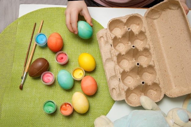 Child's hand is going to put colored Easter eggs into an empty basket