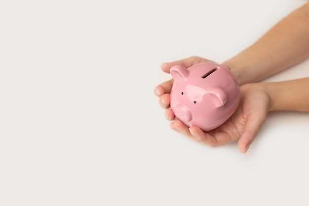 Child's hand is holding a white piggy bank on white background Saving money concept