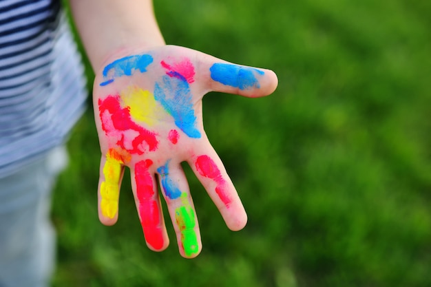 A child's hand is soiled in multicolored finger paints close-up on a grass background.