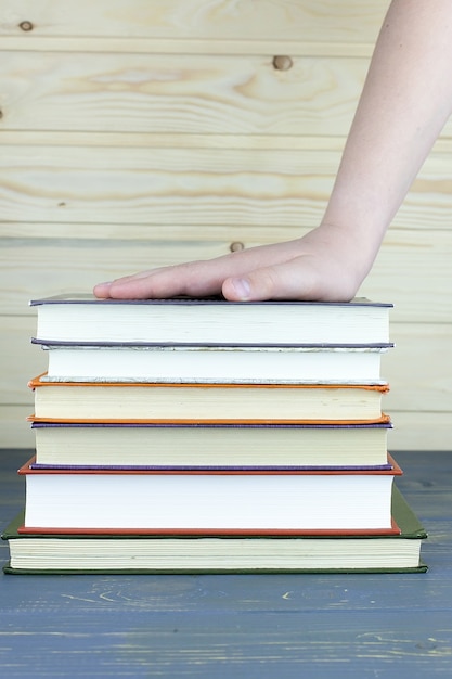 the child's hand is on a stack of books on a wooden table