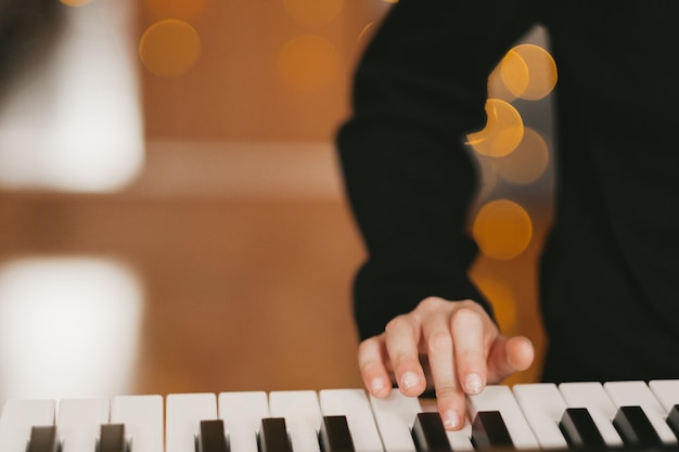 A child's hand plays the digital piano against the background of a Christmas garland The child plays the synthesizer Child's musical hobby The creative process at home