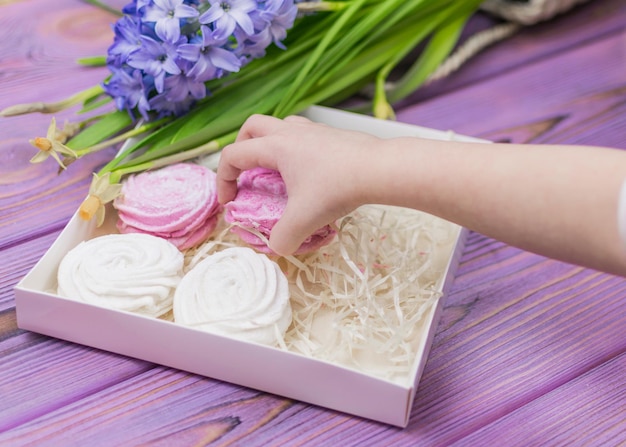 La mano del bambino tende a prendere una scatola di caramelle con uno zefiro di marshmallow Foto Premium