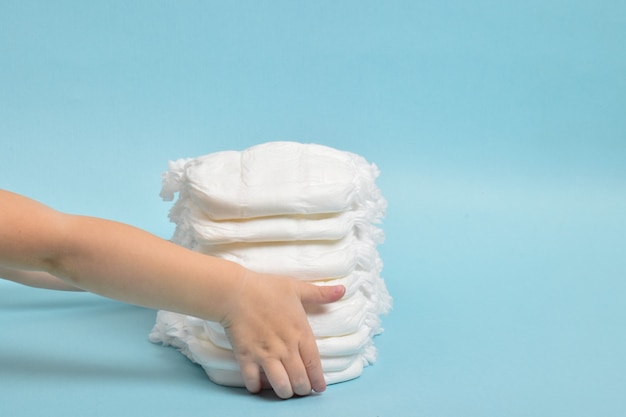 A child's hand takes a diaper-panties on a blue background.