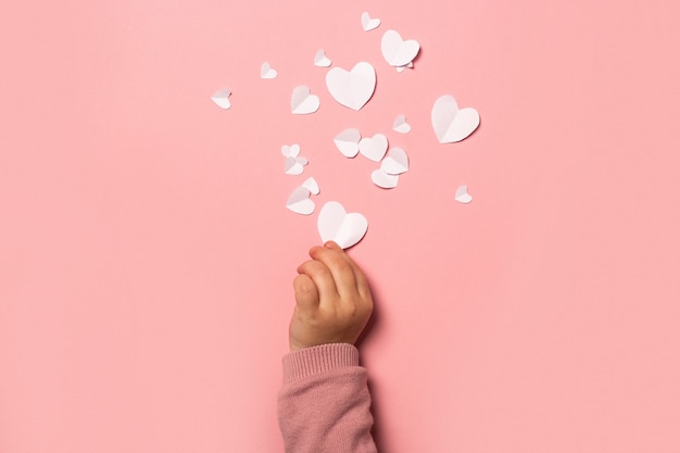 Child's hand takes a valentine card from paper on a pink background. Composition Valentine's Day. Banner. Flat lay, top view.