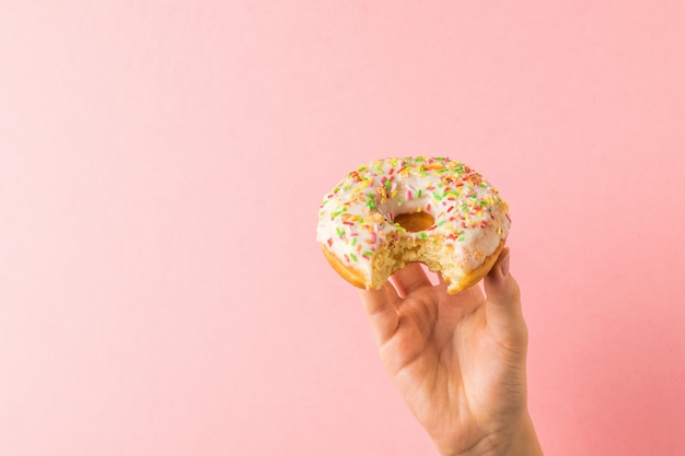 A child's hand with a nibbled donut on a light pink surface. Popular pastries.