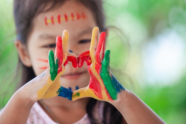 Child's hand with painted colorful watercolor make heart shape on green nature background