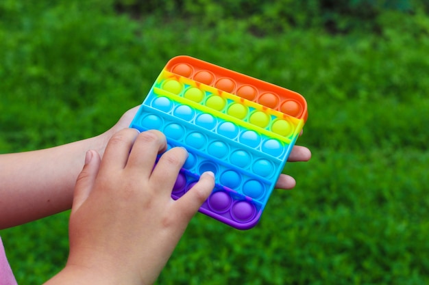 Детские руки играются квадратными разноцветными пузырями-игрушками-антистрессами сенсорными хлопками.