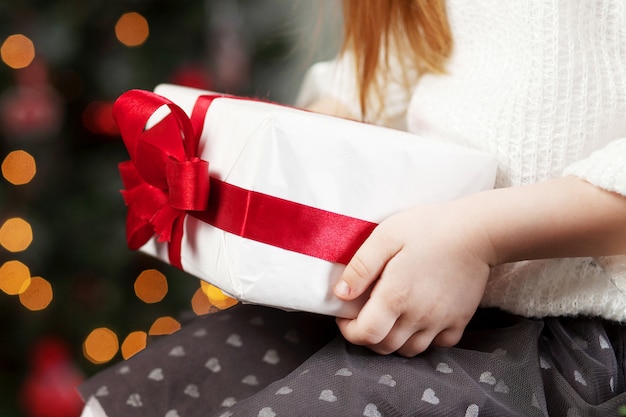 Mani del bambino che tengono il contenitore di regalo. natale, anno nuovo, concetto di compleanno. sfondo festivo con bokeh e luce solare. fiaba magica