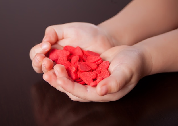 Child's hands holding red hearts on the black background.