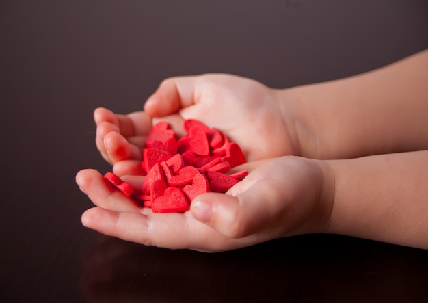 Child's hands holding red hearts on the black background.