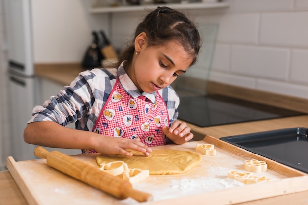 Foto mani del bambino che producono i biscotti dalla pasta cruda sotto forma di cuore, primi piani. il bambino prepara i biscotti e ritaglia delle figurine di pasta arrotolata a forma di cuore. avvicinamento.