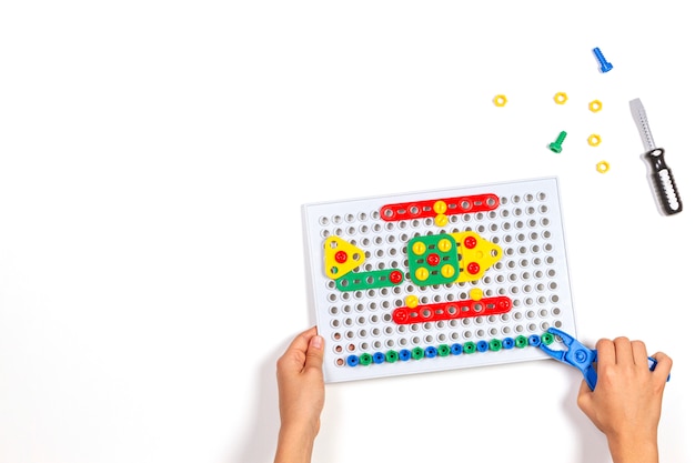 Child's hands playing with colorful toys tools on the white table. Top view