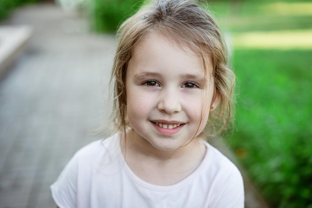 背景の緑の草に対して明るいTシャツのクローズアップで子供の肖像画の女の子